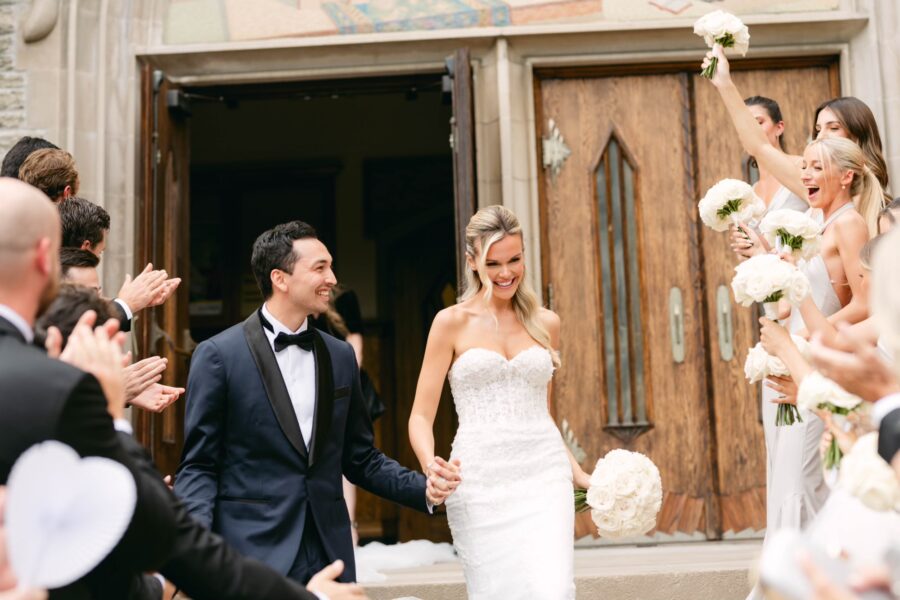 Bride and groom exiting the church after the ceremony with the wedding party on both sides of them. all white rose bouquets.