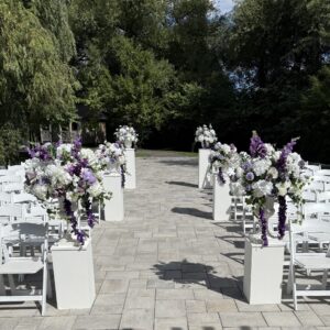 White plinths in 3 different sizes set in the aisle for the wedding ceremony with lavender, purple and white flowers
