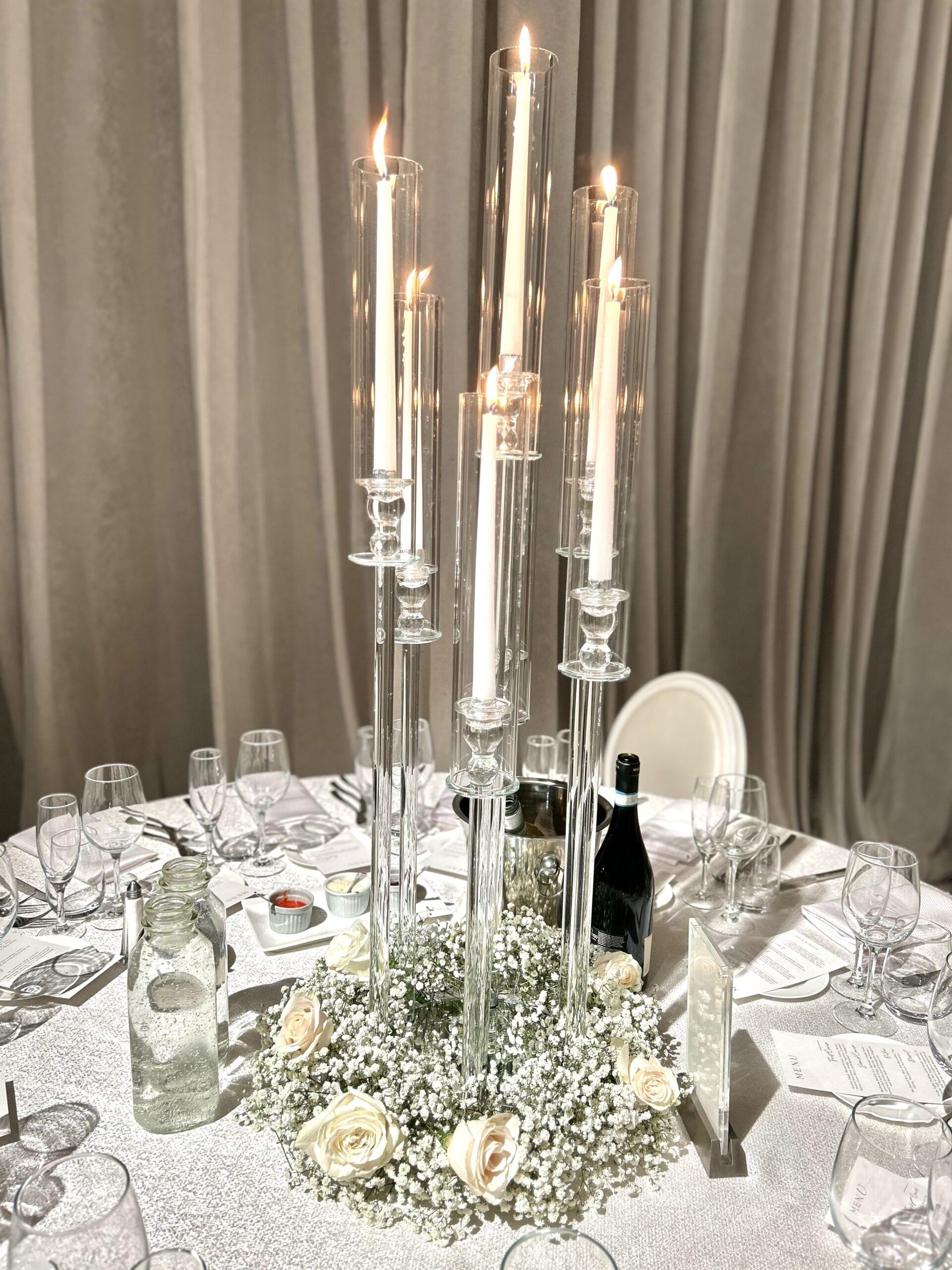 Clear 7 head candelabras with candles and white roses and baby's breath at the base on guest table for wedding reception