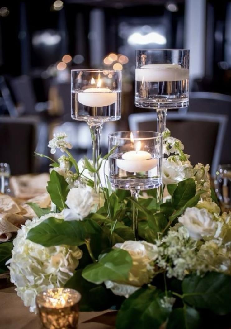 Monet candle holders with floating candles for rent with white florals and greenery at the base